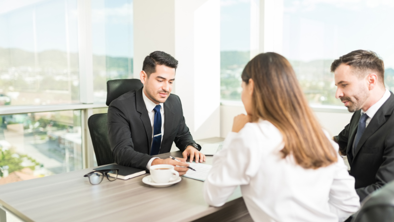 A financial advisor discussing rebridging options with a couple, explaining how they can refinance their bridging loan after a failed exit strategy