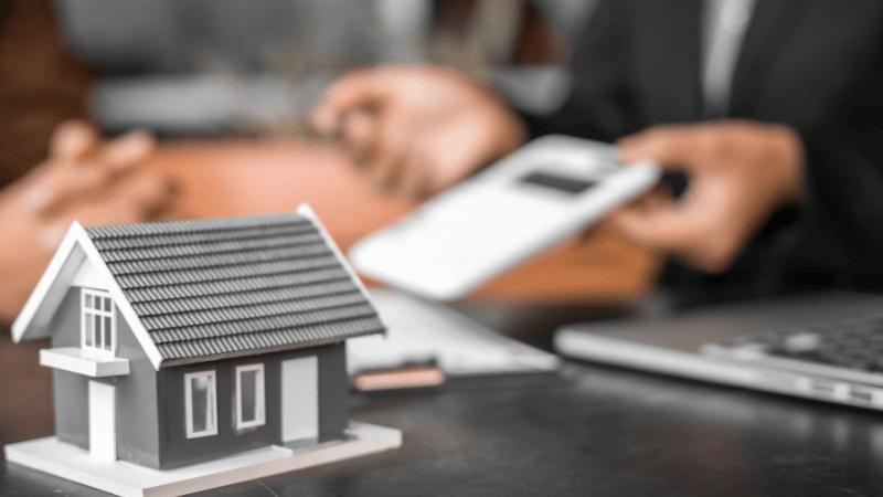 A person's hands placing small wooden model houses on a desk next to financial documents, symbolizing the process of building a property portfolio with the BRRRR method.