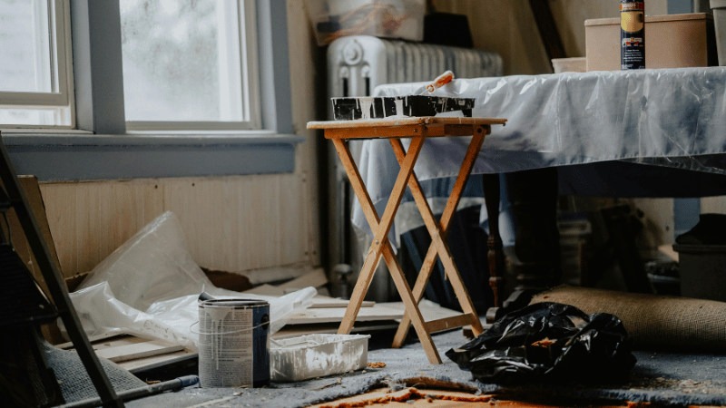 A cluttered room in the middle of a DIY home improvement project, with paint supplies and dust sheets, representing renovations that may not add value.