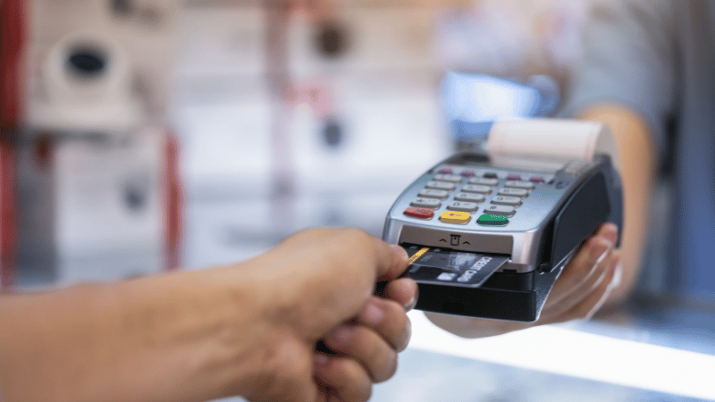 A close-up of a person using a credit card machine to make a payment in a retail environment, representing a typical business that uses merchant cash advance.